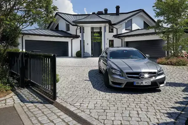 Modernes Einfamilienhaus mit luxuriösem Mercedes auf gepflasterter Einfahrt und Tor.